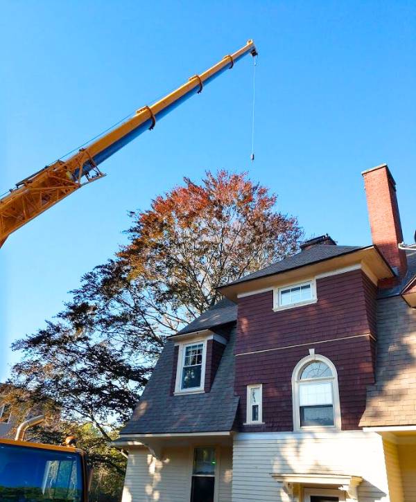 Orange crane in front of a property ready to lift a cut off tree by Regal tree and shrub experts.